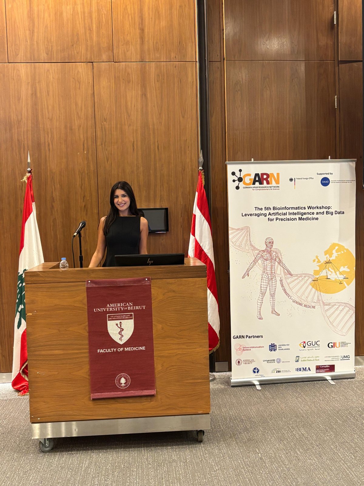 Perla Makhoul presenting at a podium at the American University of Beirut, next to the GARN bioinformatics workshop banner