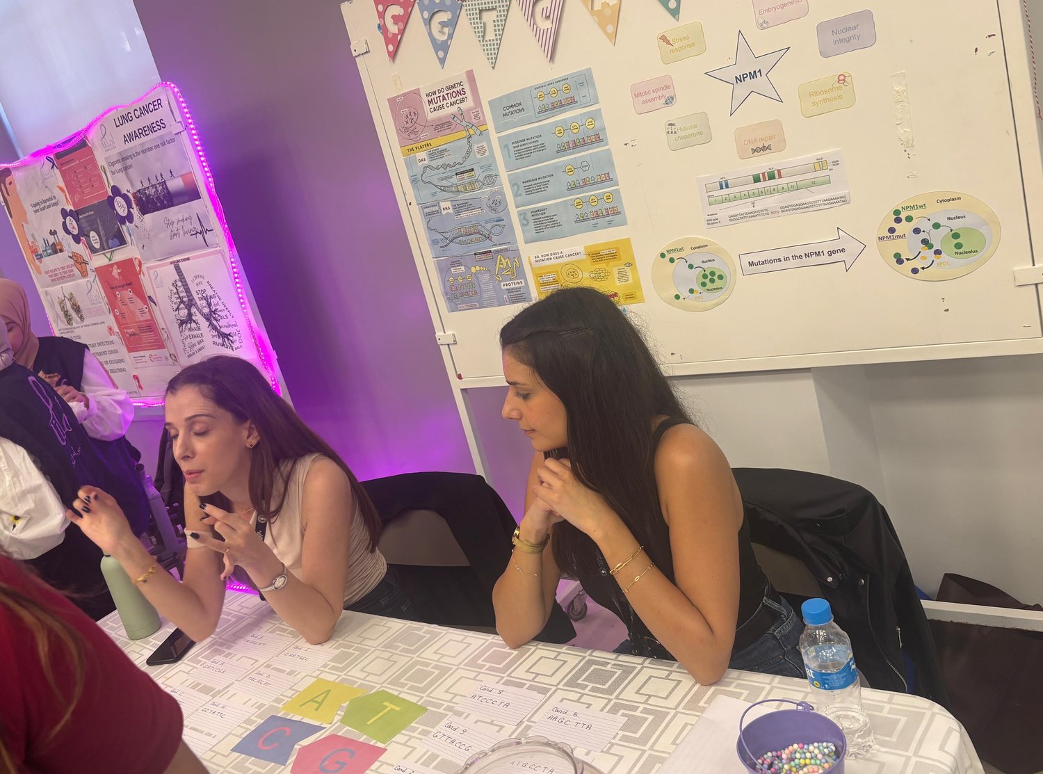 Perla Makhoul at the science booth during AUB STEM Week, seated at a table of activity cards in front of a display board